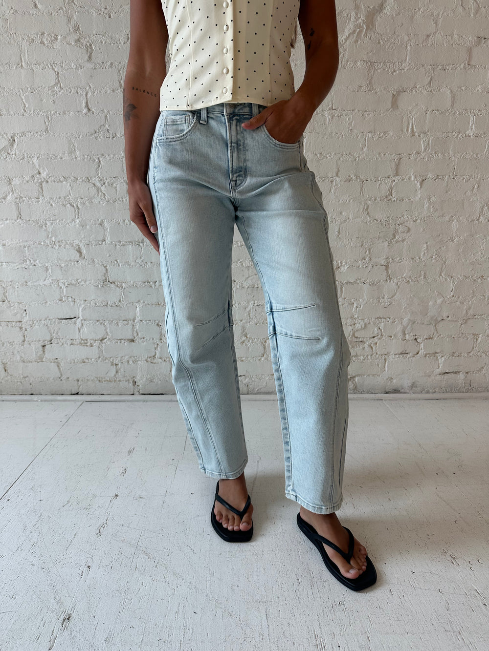 Woman wearing light wash barrel jean with front seam detail and polka dot halter top.