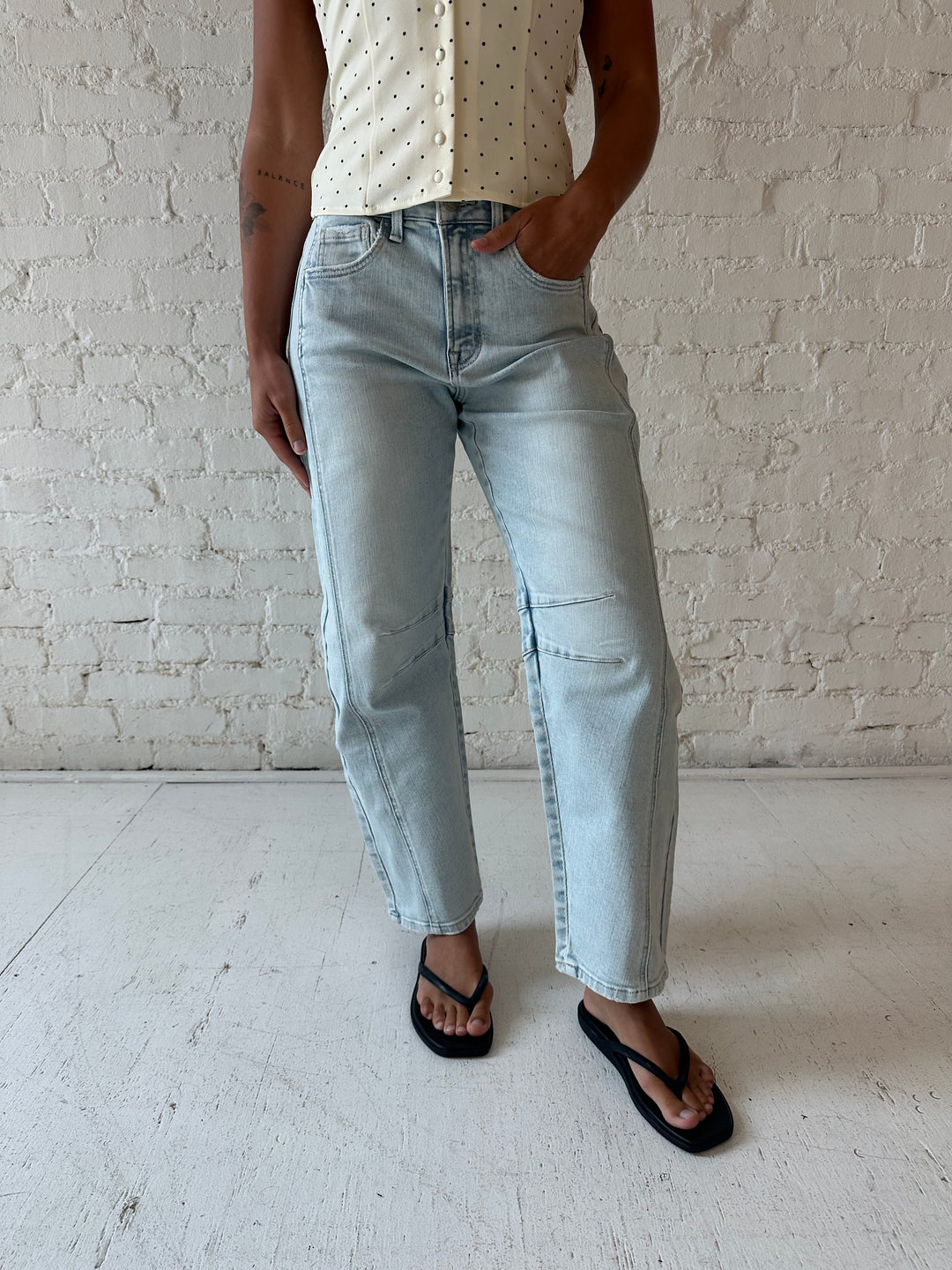 Woman wearing light wash barrel jean with front seam detail and polka dot halter top.