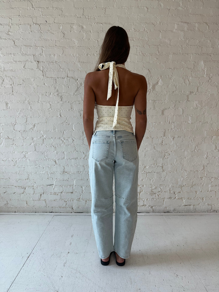 Woman wearing light wash barrel jean with front seam detail and polka dot halter top.