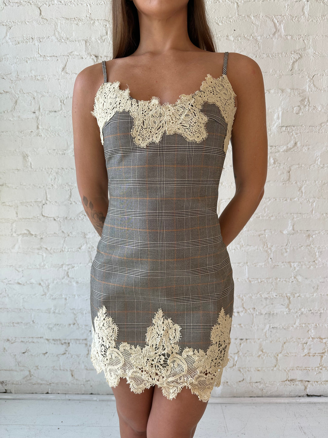 Woman wearing taupe plaid mini dress with lace trim detail and adjustable straps.
