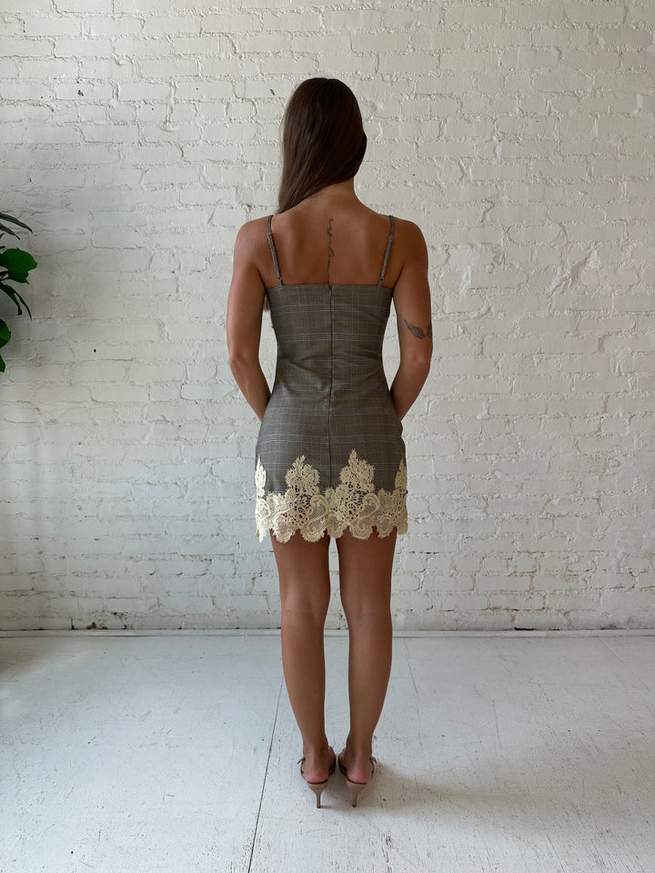 Woman wearing taupe plaid mini dress with lace trim detail and adjustable straps.