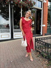 Woman wearing red cowl neck satin midi dress with polka dot pattern. 