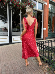 Woman wearing red cowl neck satin midi dress with polka dot pattern. 