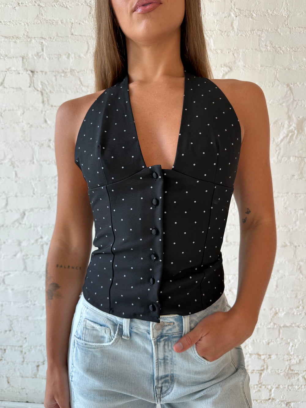 Woman wearing black polka dot halter top with light wash barrel jean.