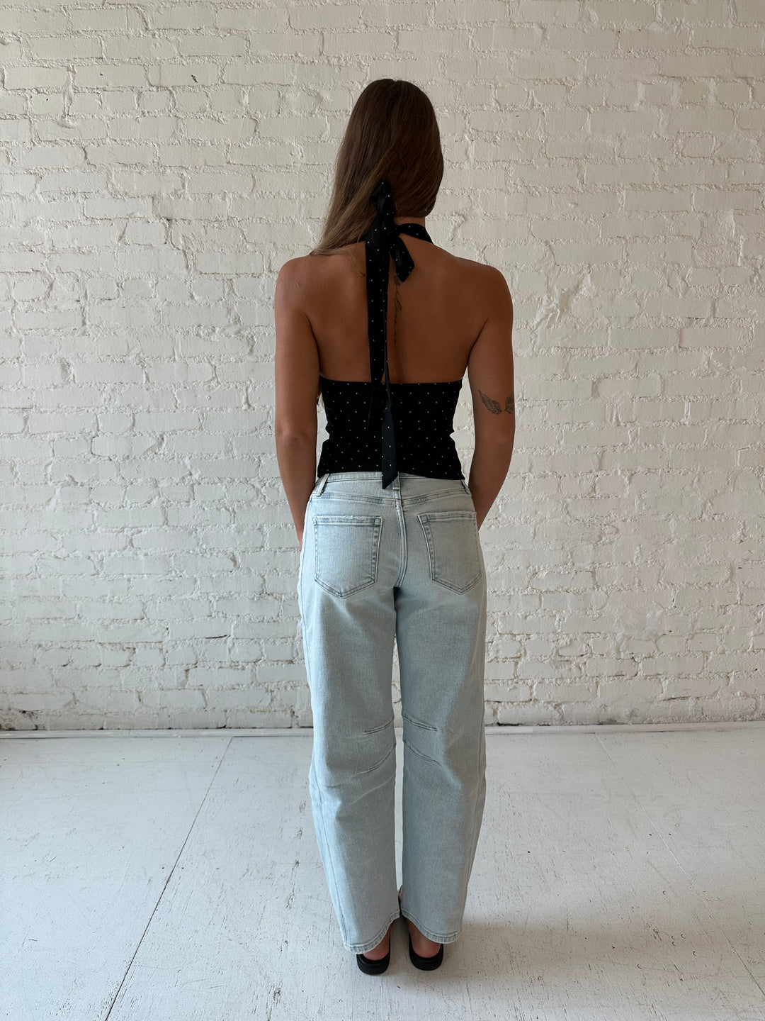 Woman wearing black polka dot halter top with light wash barrel jean.