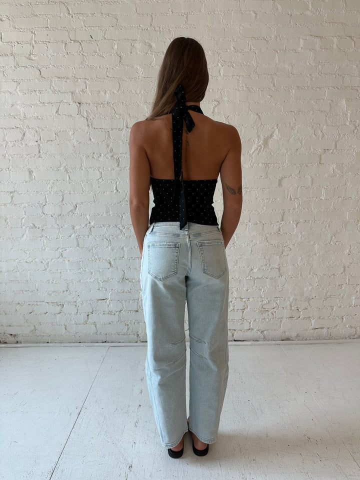 Woman wearing black polka dot halter top with light wash barrel jean.