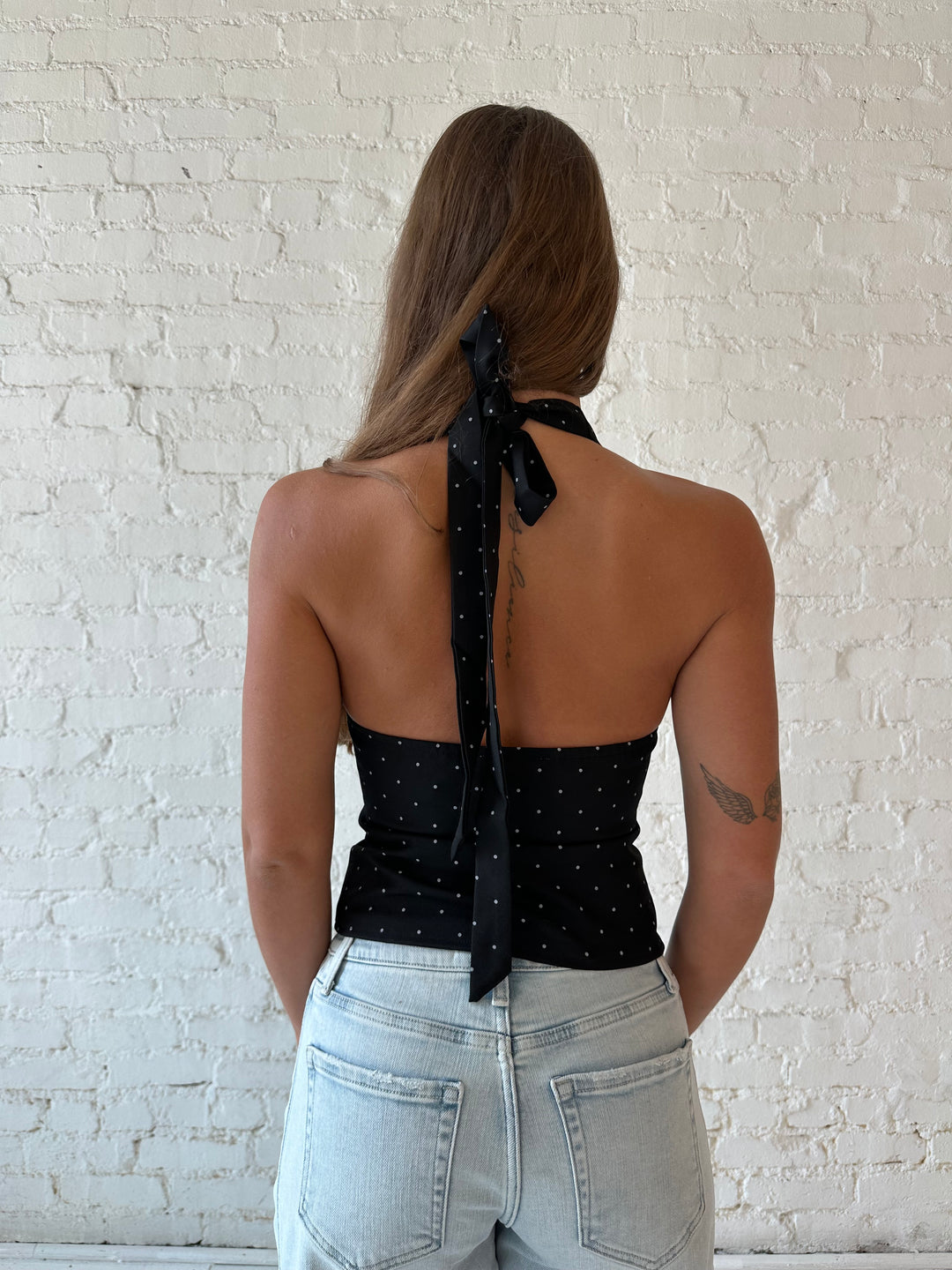 Woman wearing black polka dot halter top with light wash barrel jean.