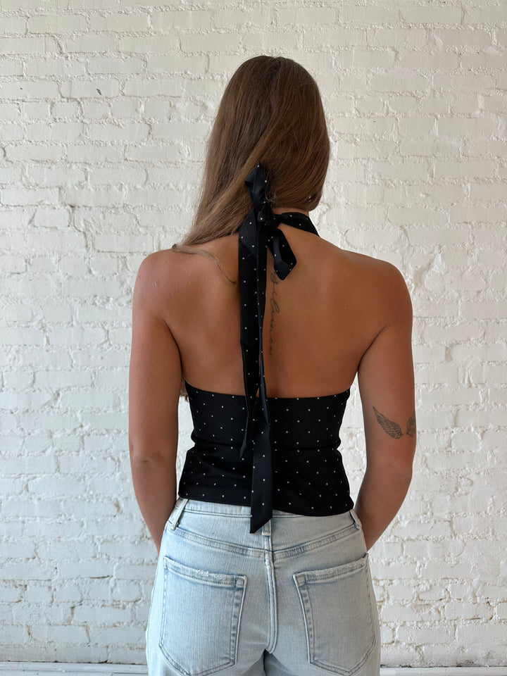 Woman wearing black polka dot halter top with light wash barrel jean.