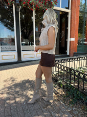 Woman wearing oatmeal colored chunky sleeveless sweater with front tie closure. 