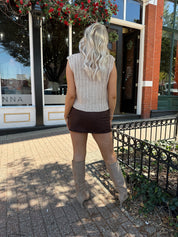 Woman wearing oatmeal colored chunky sleeveless sweater with front tie closure. 