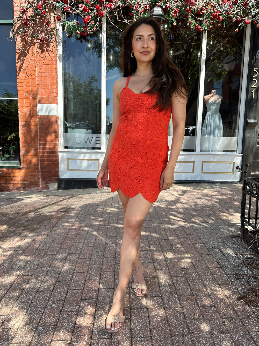 Woman wearing coral red crochet mini dress with adjustable straps, and scallop hem.
