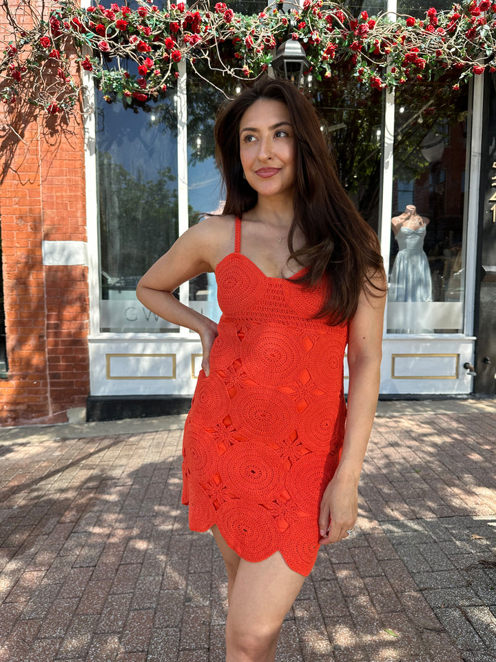 Woman wearing coral red crochet mini dress with adjustable straps, and scallop hem.