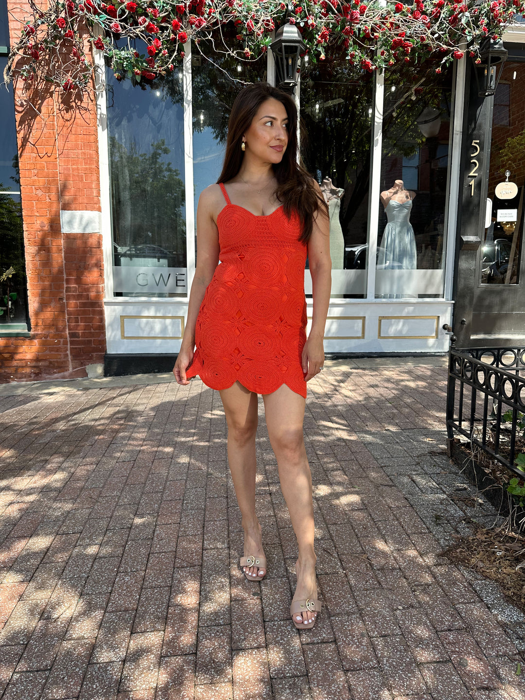 Woman wearing coral red crochet mini dress with adjustable straps, and scallop hem.
