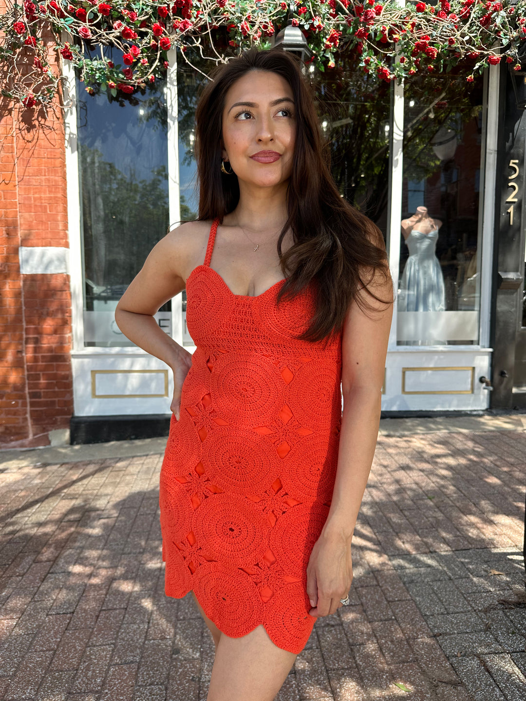 Woman wearing coral red crochet mini dress with adjustable straps, and scallop hem.