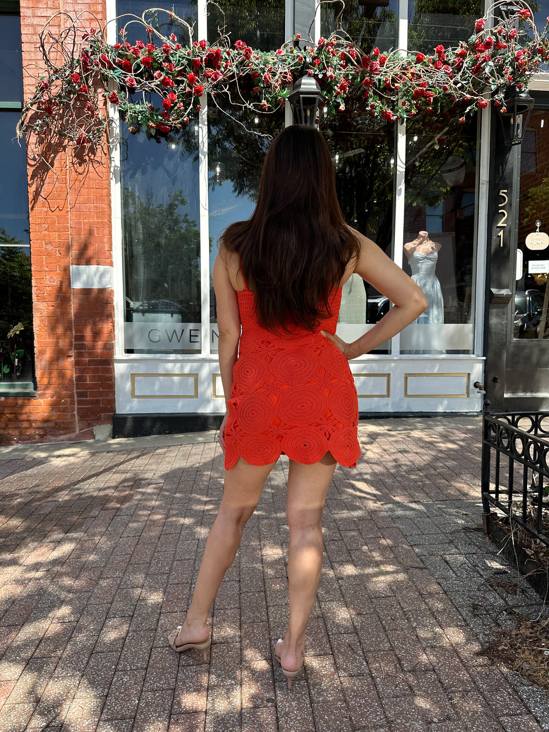 Woman wearing coral red crochet mini dress with adjustable straps, and scallop hem.