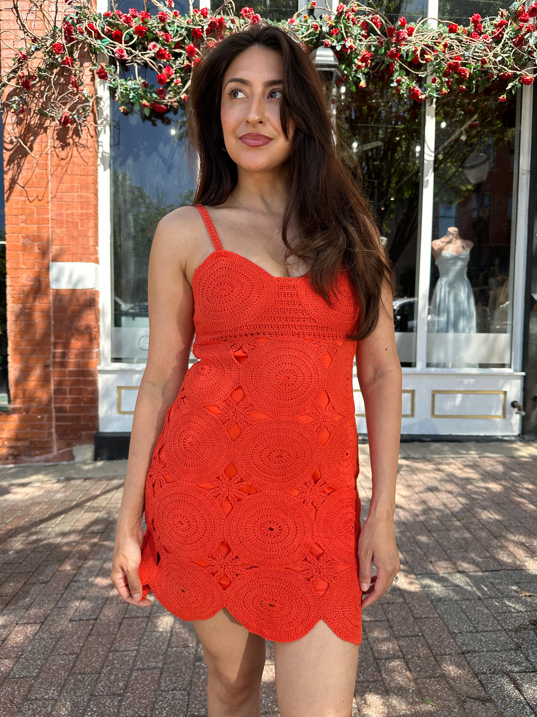 Woman wearing coral red crochet mini dress with adjustable straps, and scallop hem.