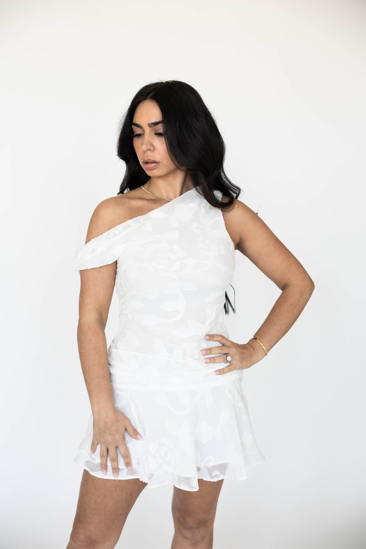 Woman wearing white jacquard draped mini dress with an off the shoulder neckline. 