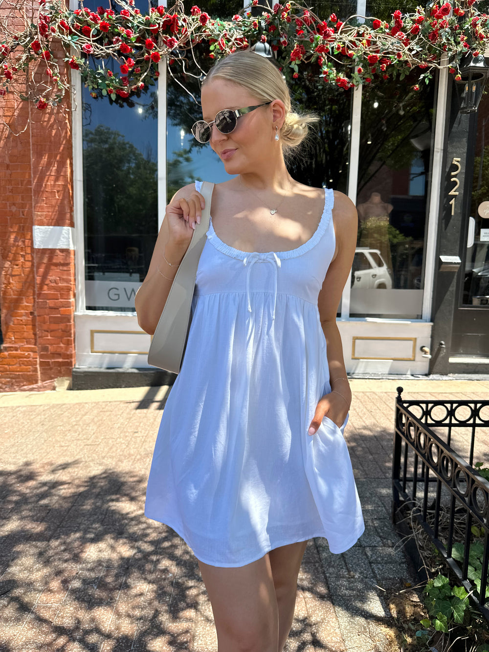 Woman wearing white mini dress with scoop neckline, ruffle trim, and functional pockets. 