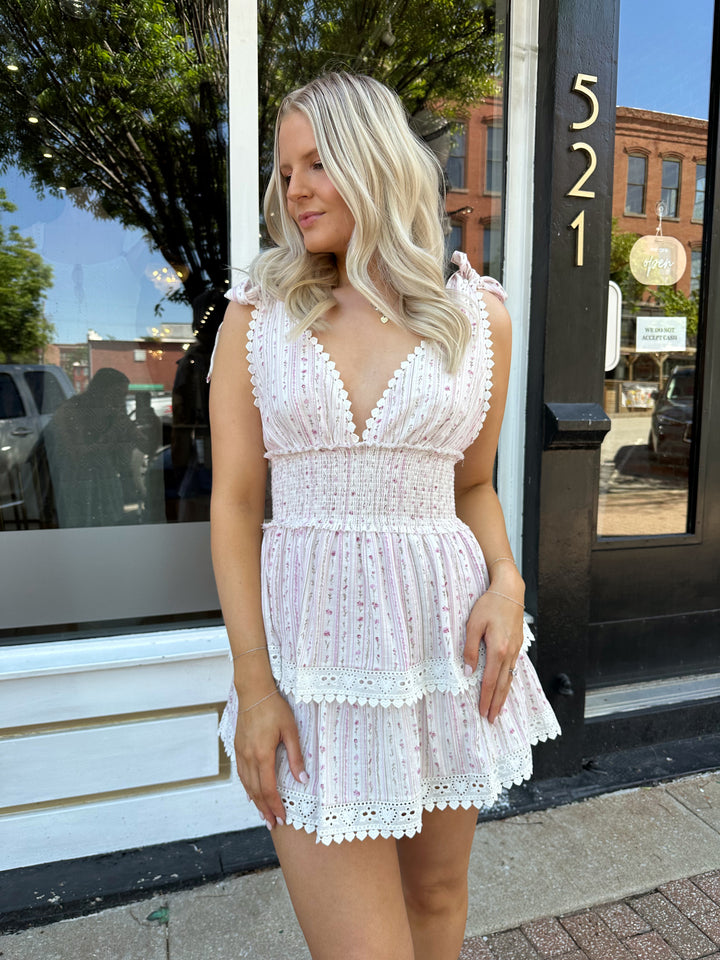 Woman wearing pink floral tiered mini dress with self tie straps, and v-neckline. 