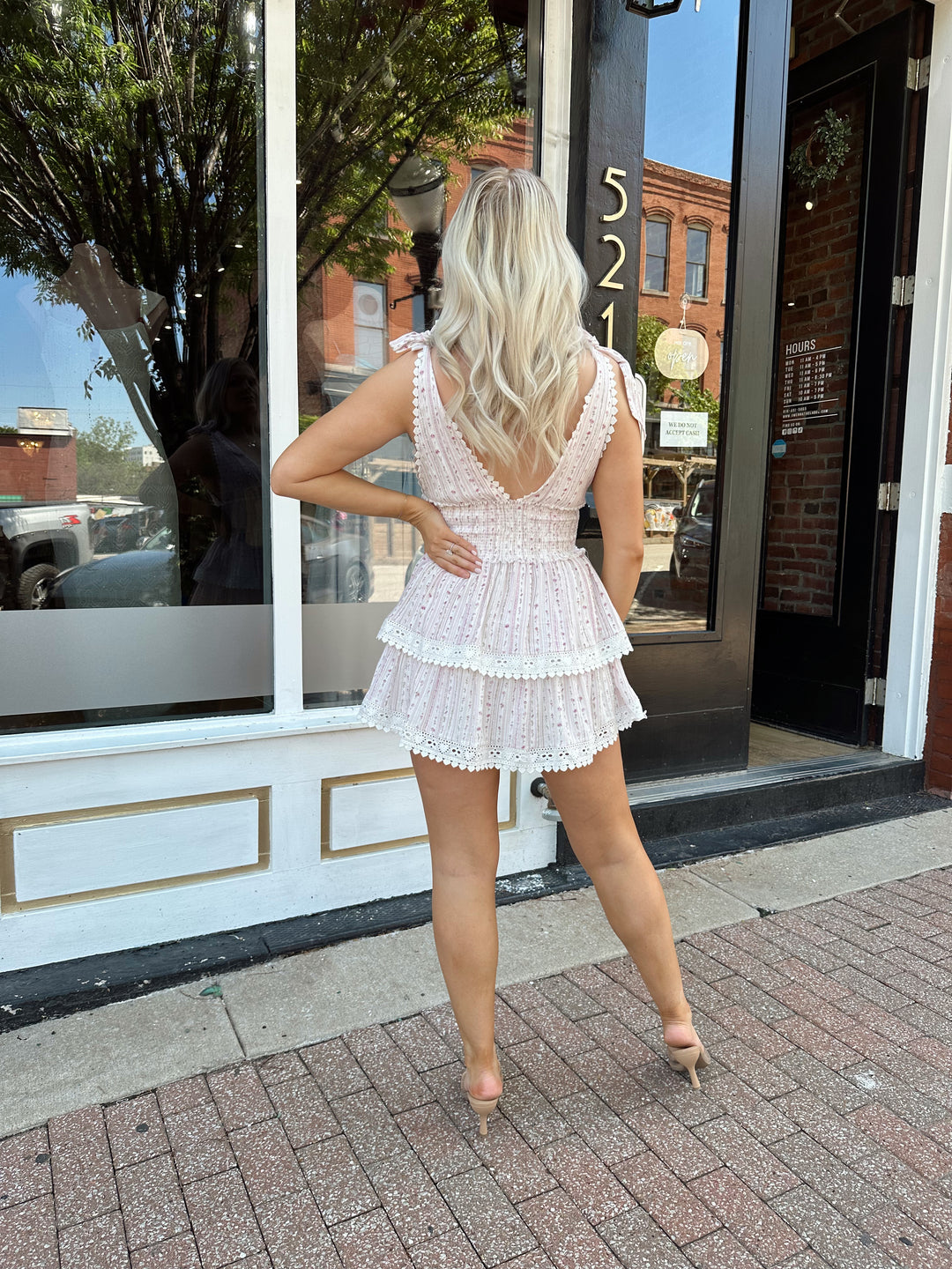 Woman wearing pink floral tiered mini dress with self tie straps, and v-neckline. 