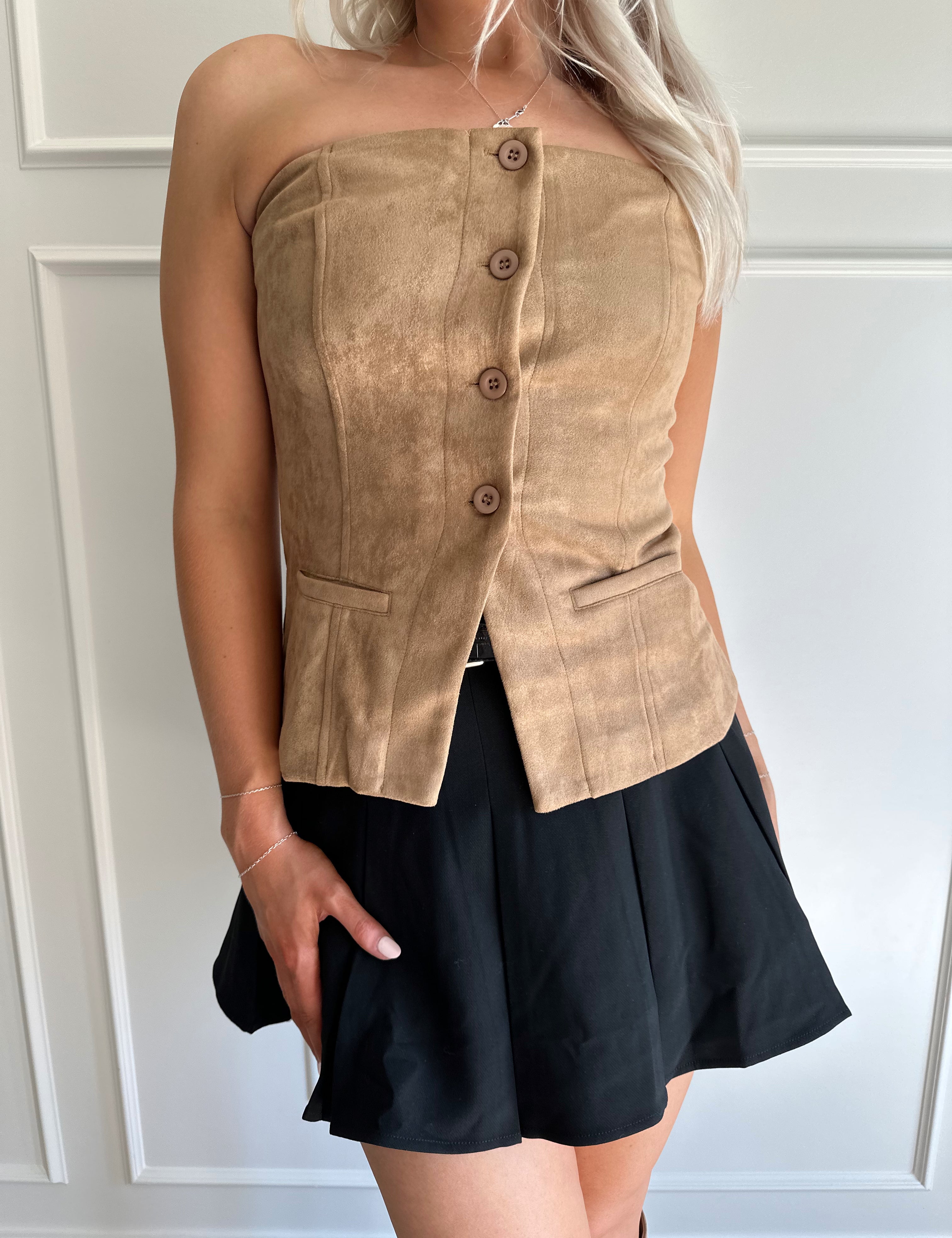 Woman wearing tan suede strapless top with front button closure and faux pockets. 