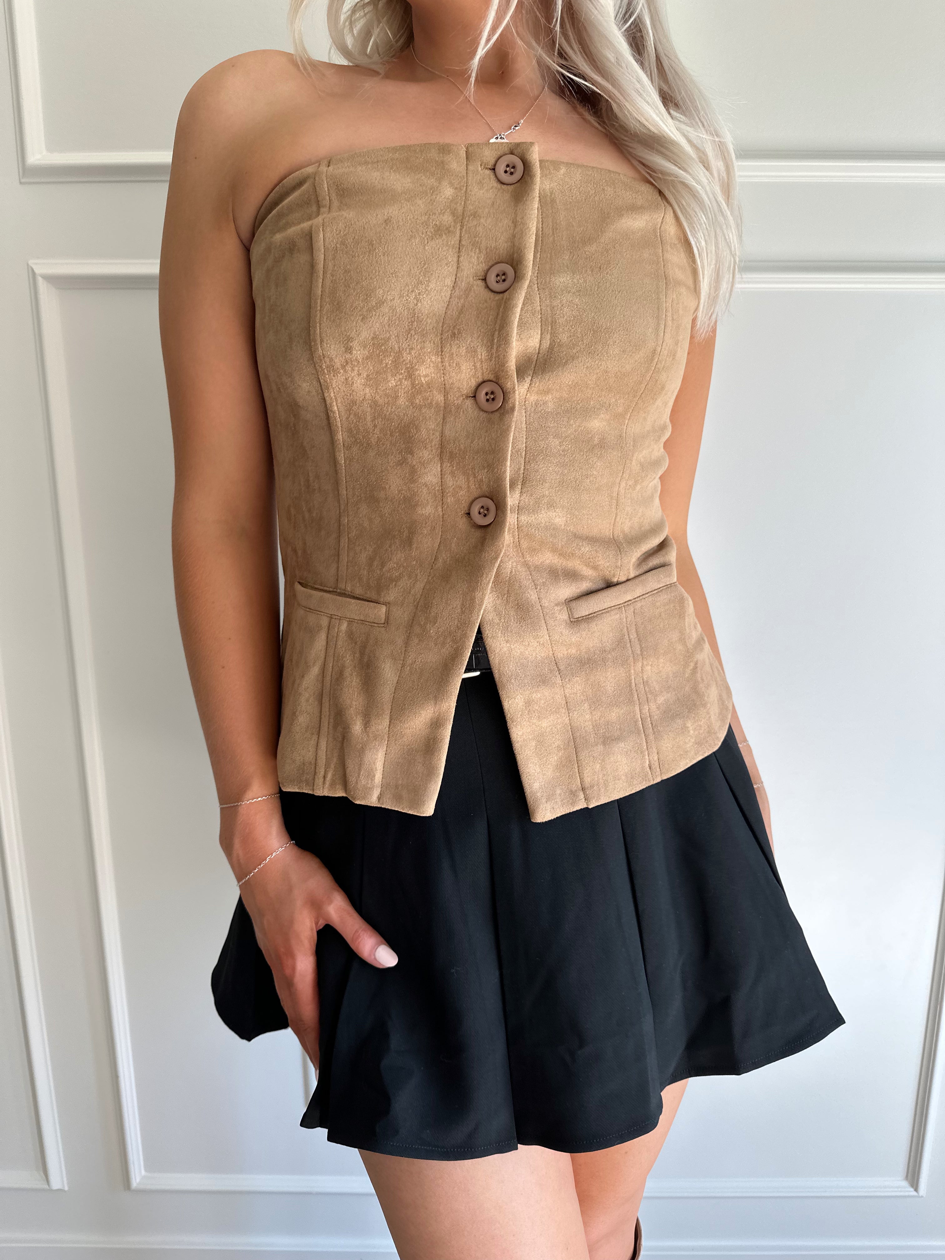 Woman wearing tan suede strapless top with front button closure and faux pockets. 