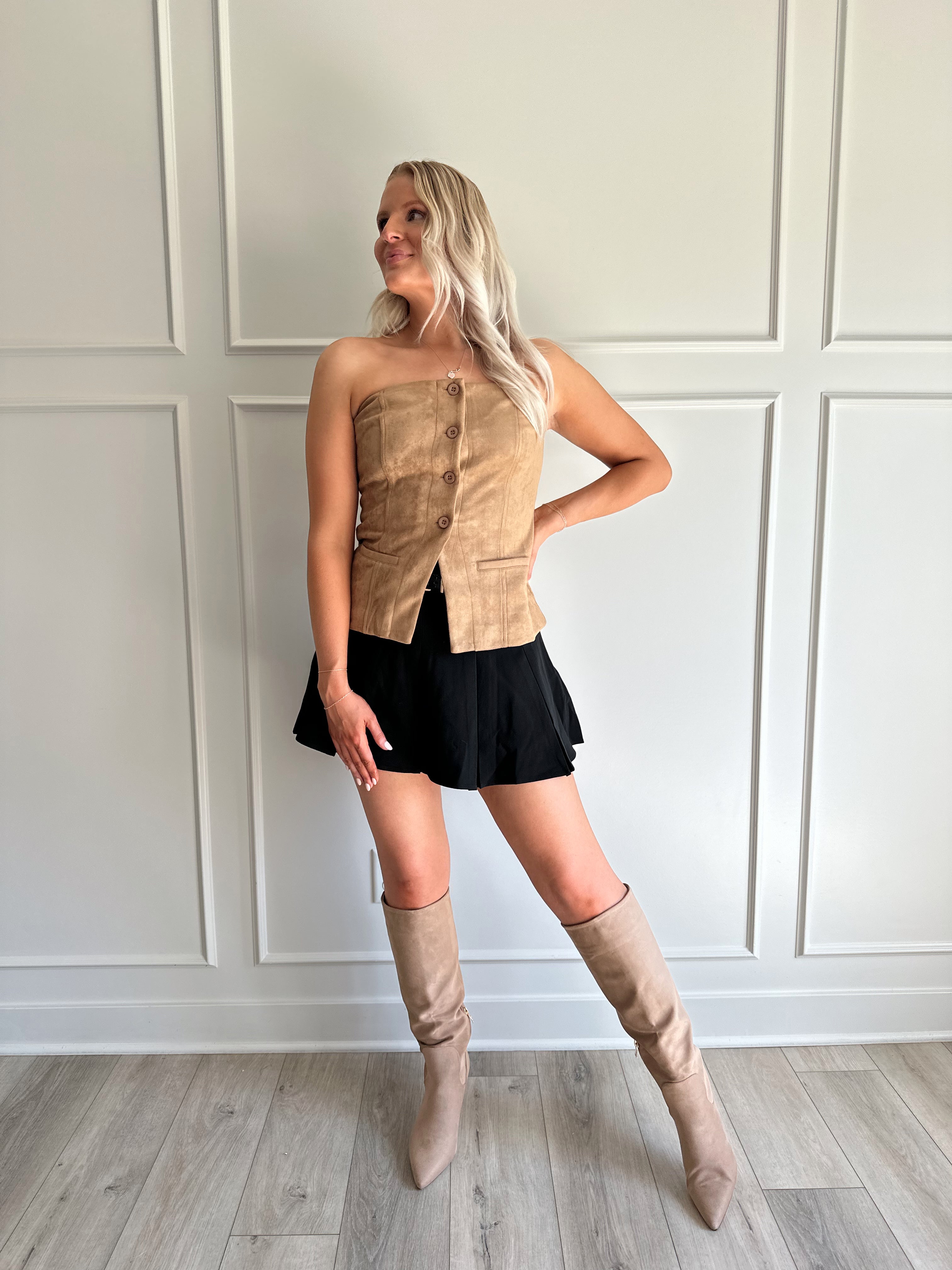 Woman wearing tan suede strapless top with front button closure and faux pockets. 