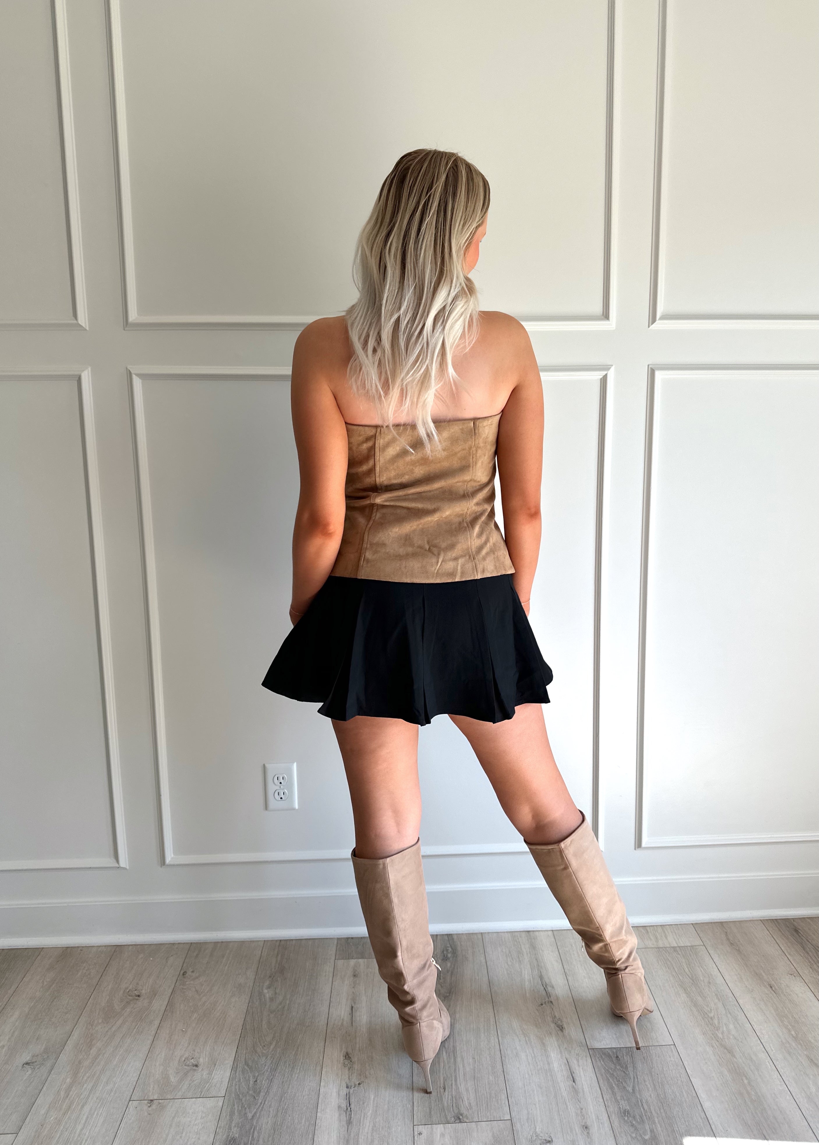 Woman wearing tan suede strapless top with front button closure and faux pockets. 