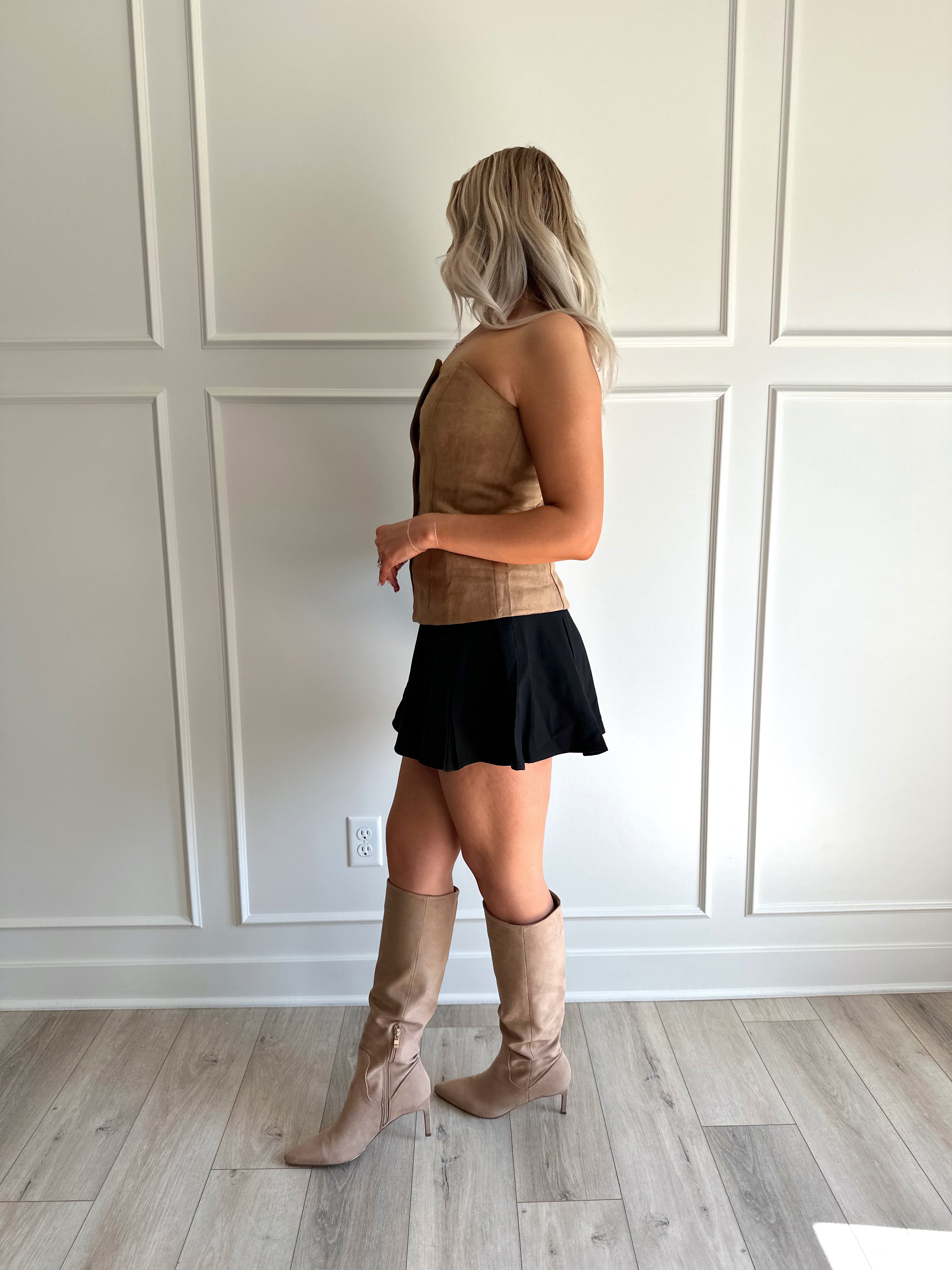 Woman wearing tan suede strapless top with front button closure and faux pockets. 