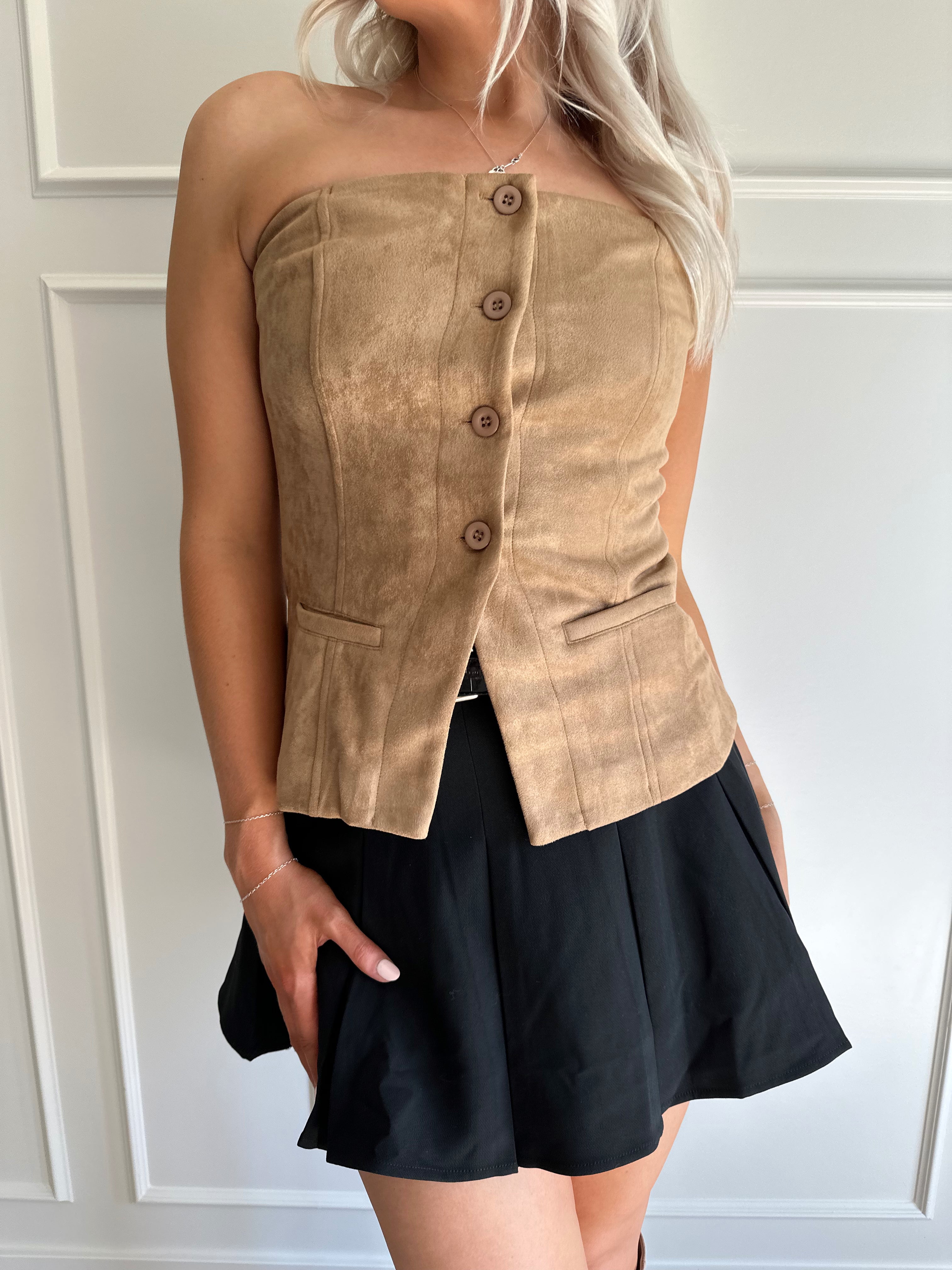 Woman wearing tan suede strapless top with front button closure and faux pockets. 