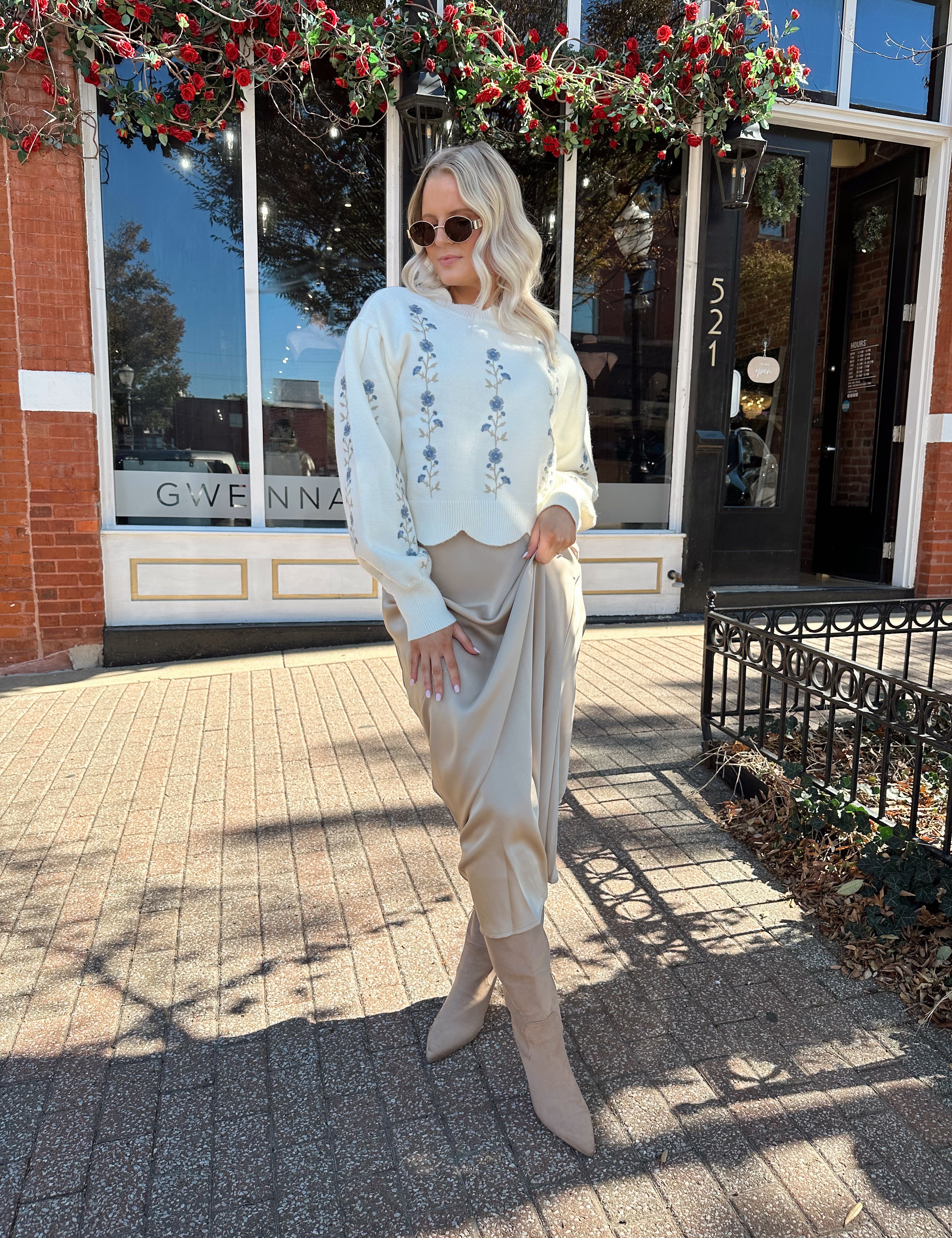 Woman wearing cream sweater with blue embroidered floral pattern. 