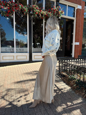 Woman wearing cream sweater with blue embroidered floral pattern. 