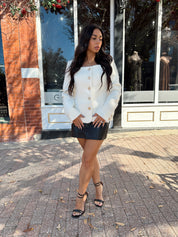 Woman wearing cream bouclé long sleeve jacket with gold button closure.