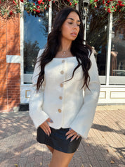 Woman wearing cream bouclé long sleeve jacket with gold button closure.