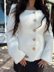 Woman wearing cream bouclé long sleeve jacket with gold button closure.