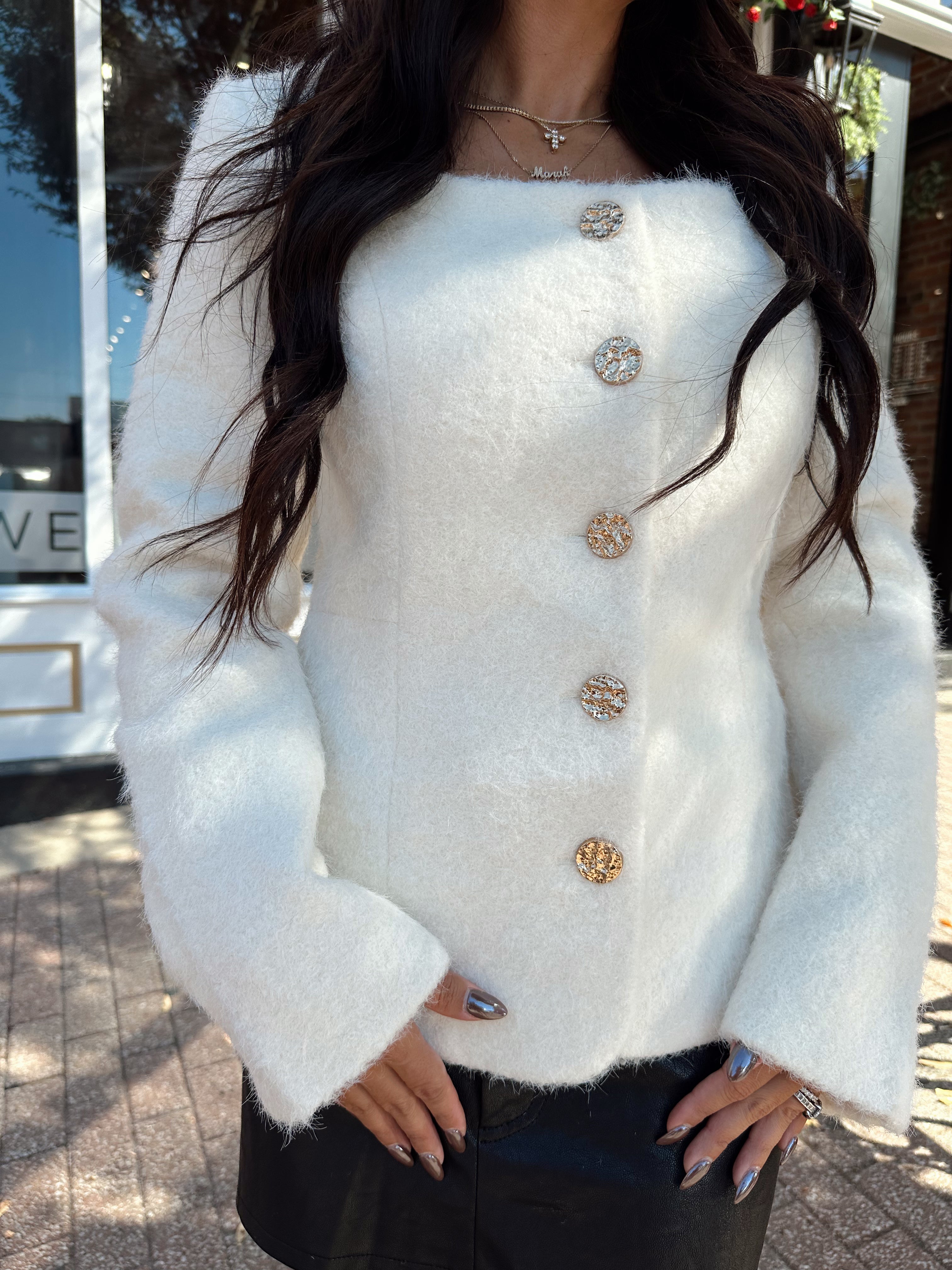 Woman wearing cream bouclé long sleeve jacket with gold button closure.
