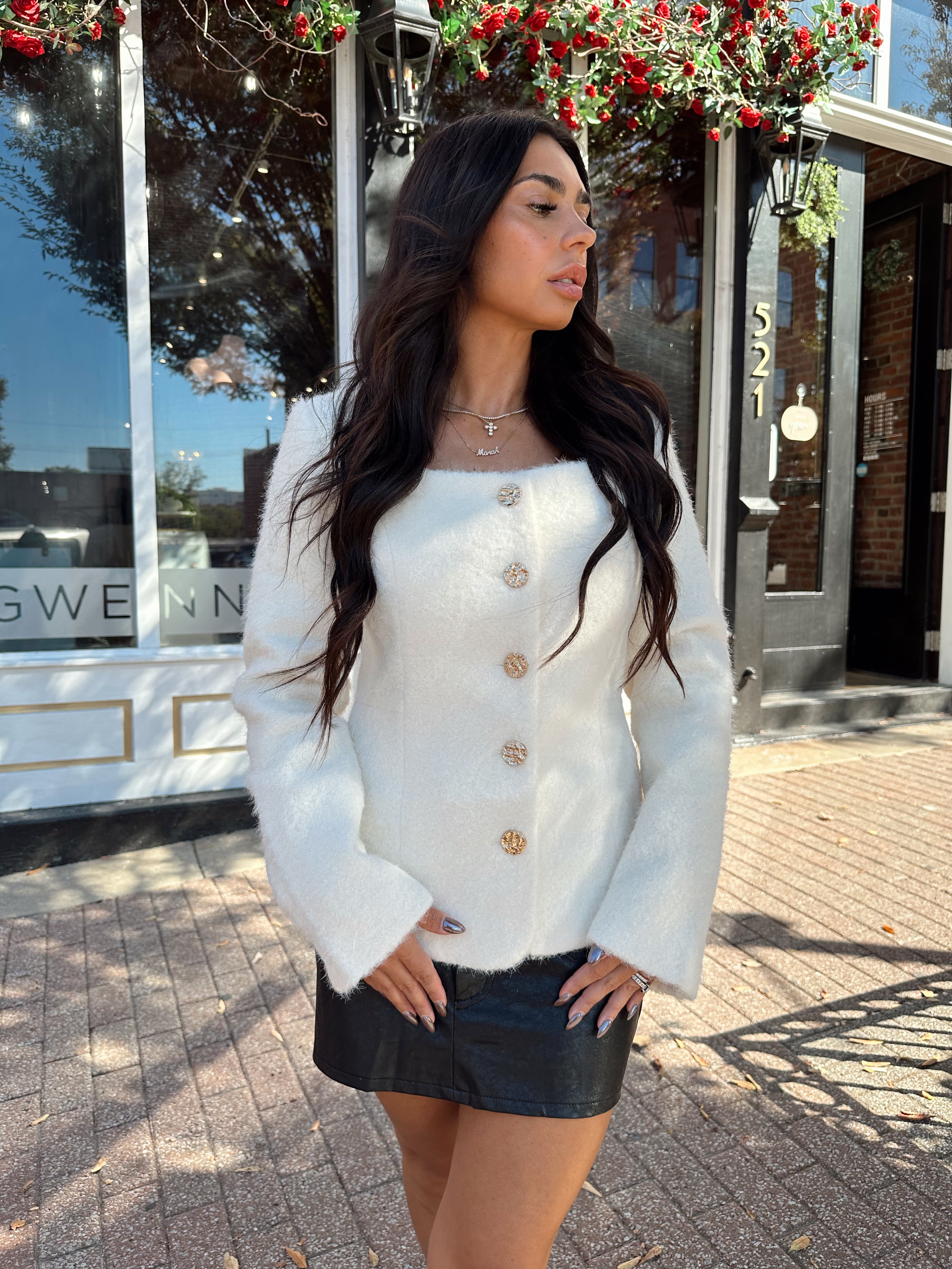 Woman wearing cream bouclé long sleeve jacket with gold button closure.