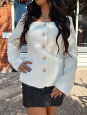 Woman wearing cream bouclé long sleeve jacket with gold button closure.