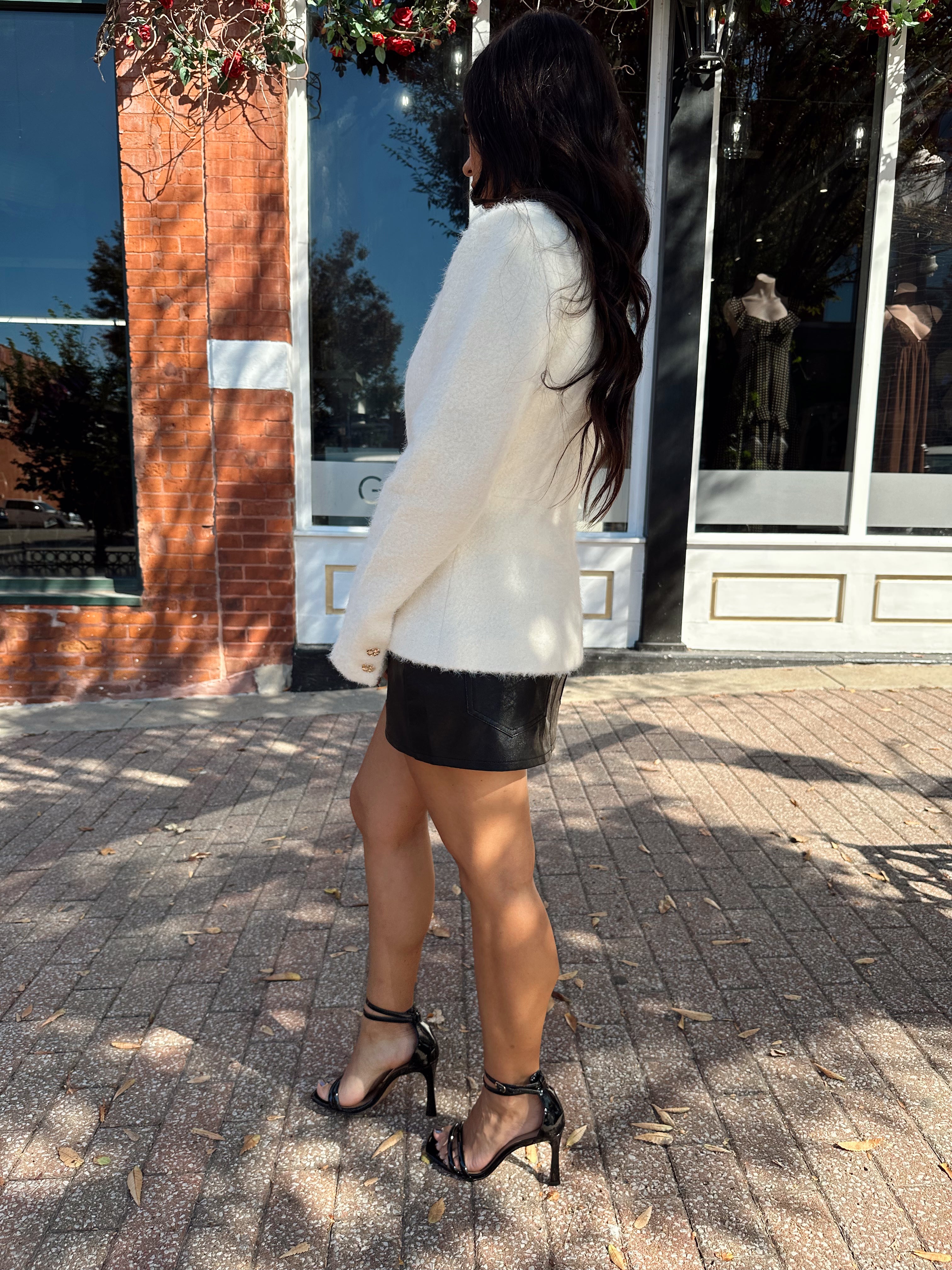Woman wearing cream bouclé long sleeve jacket with gold button closure.