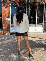 Woman wearing cream bouclé long sleeve jacket with gold button closure.