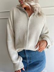 Woman wearing a taupe knit oversized jacket and denim mini skirt. 