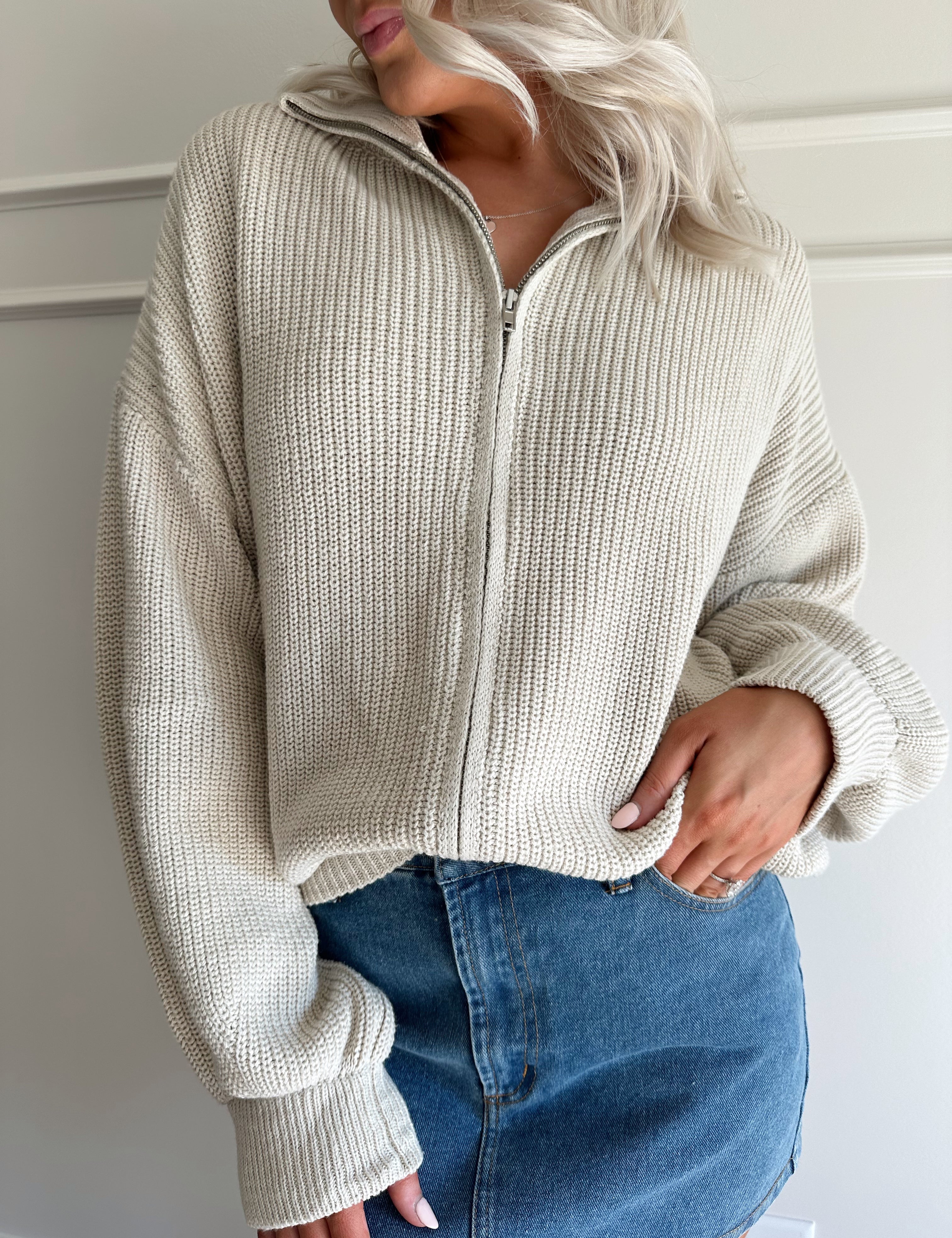 Woman wearing a taupe knit oversized jacket and denim mini skirt. 