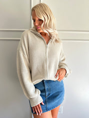 Woman wearing a taupe knit oversized jacket and denim mini skirt. 