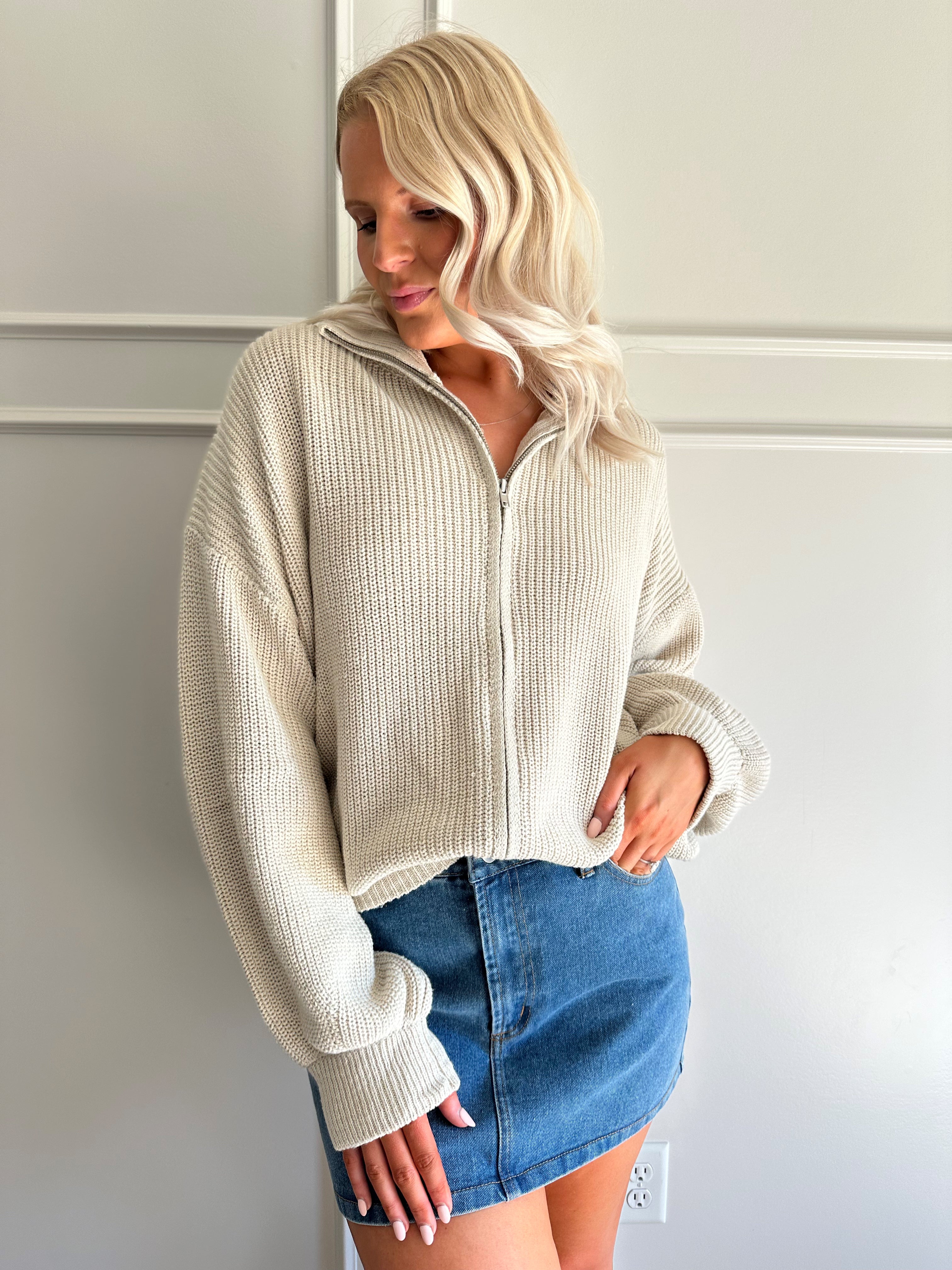 Woman wearing a taupe knit oversized jacket and denim mini skirt. 