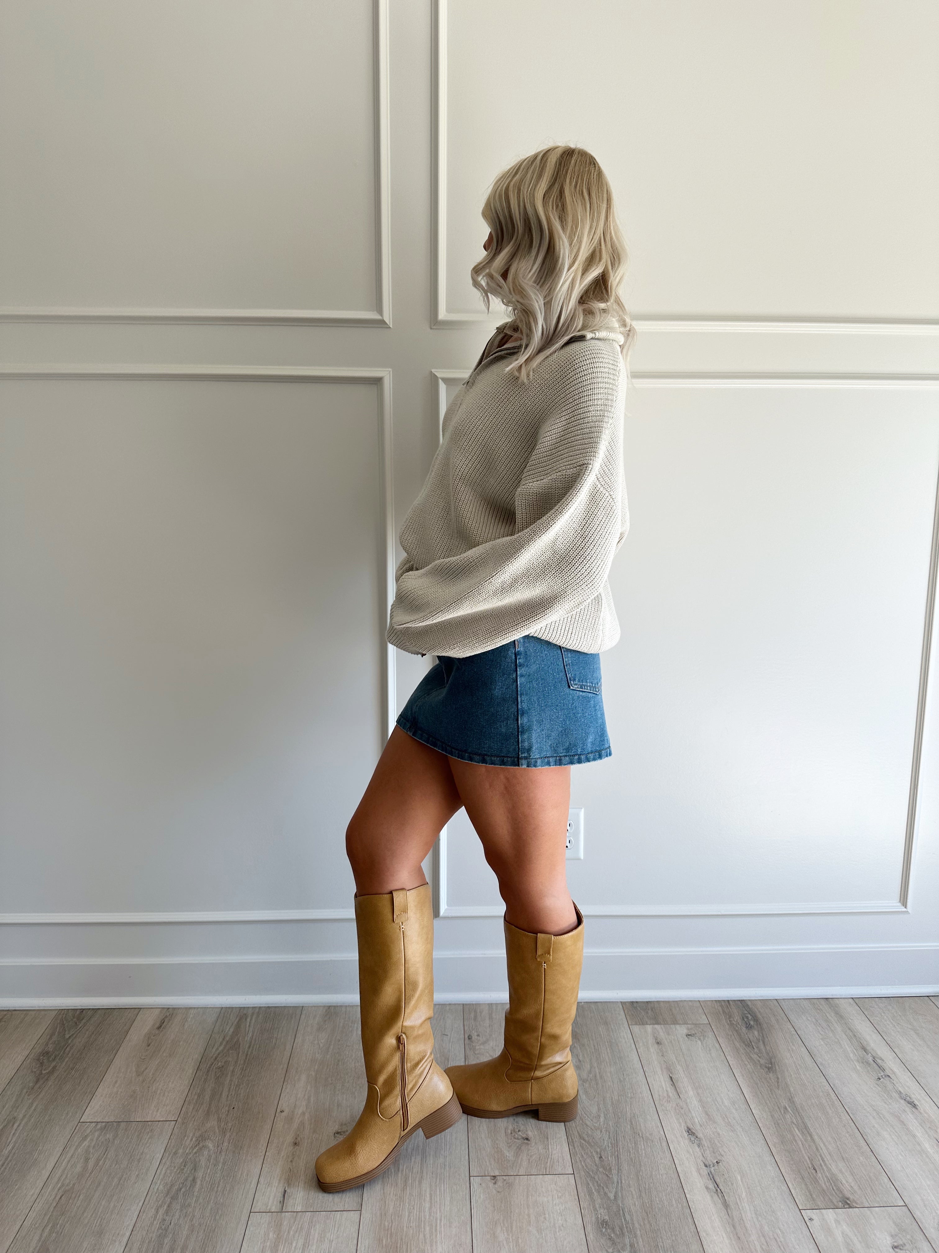 Woman wearing a taupe knit oversized jacket and denim mini skirt. 