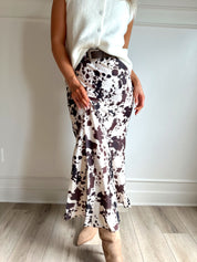 Woman wearing satin cow print maxi skirt with belt detail and white sweater top.