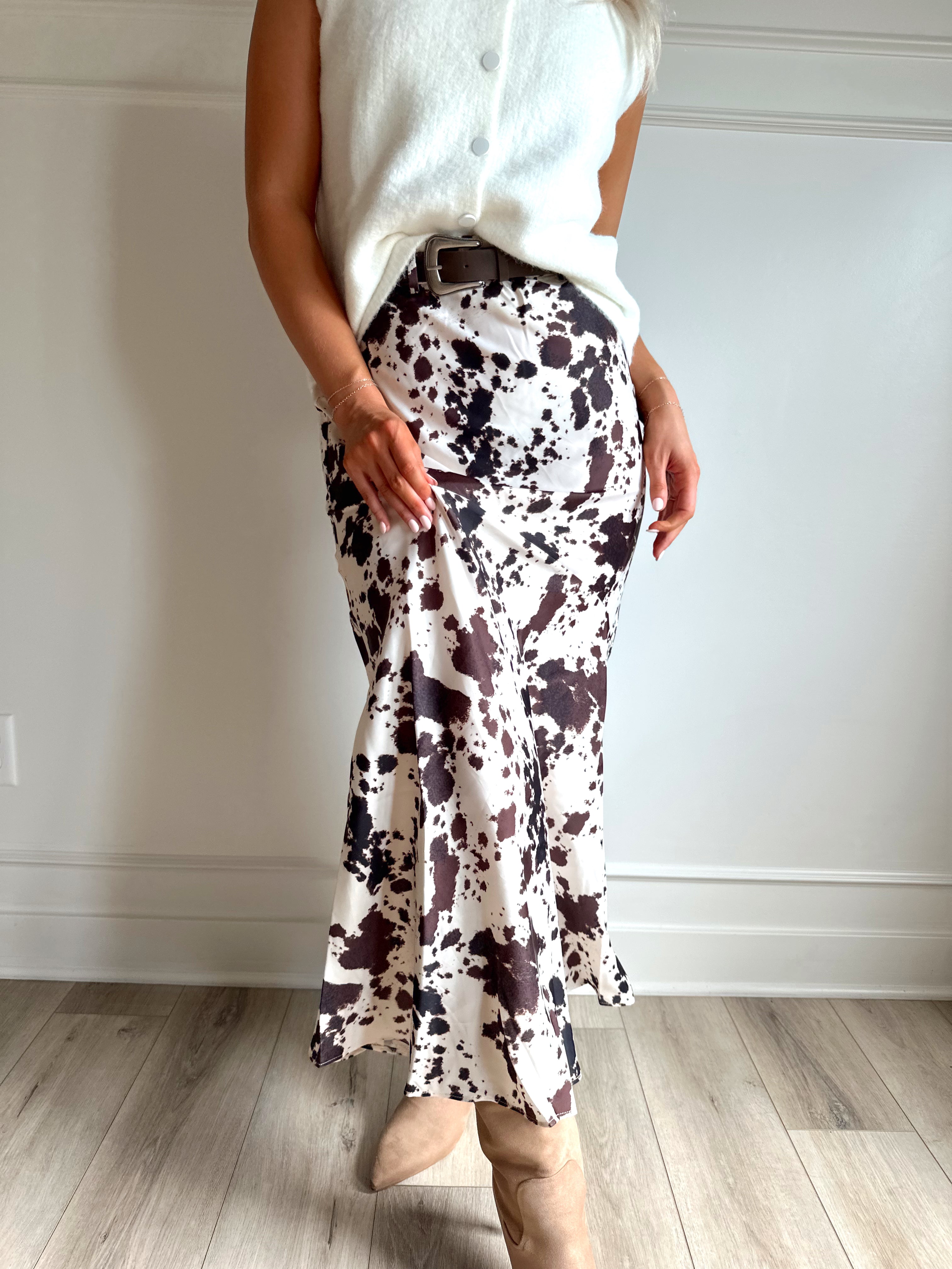 Woman wearing satin cow print maxi skirt with belt detail and white sweater top.
