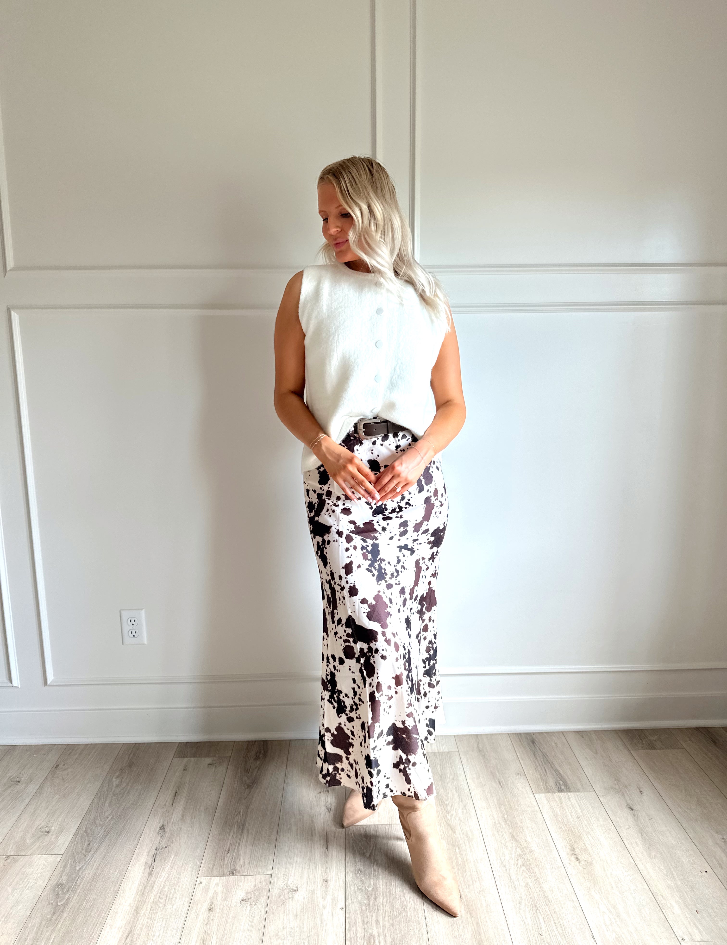 Woman wearing satin cow print maxi skirt with belt detail and white sweater top.