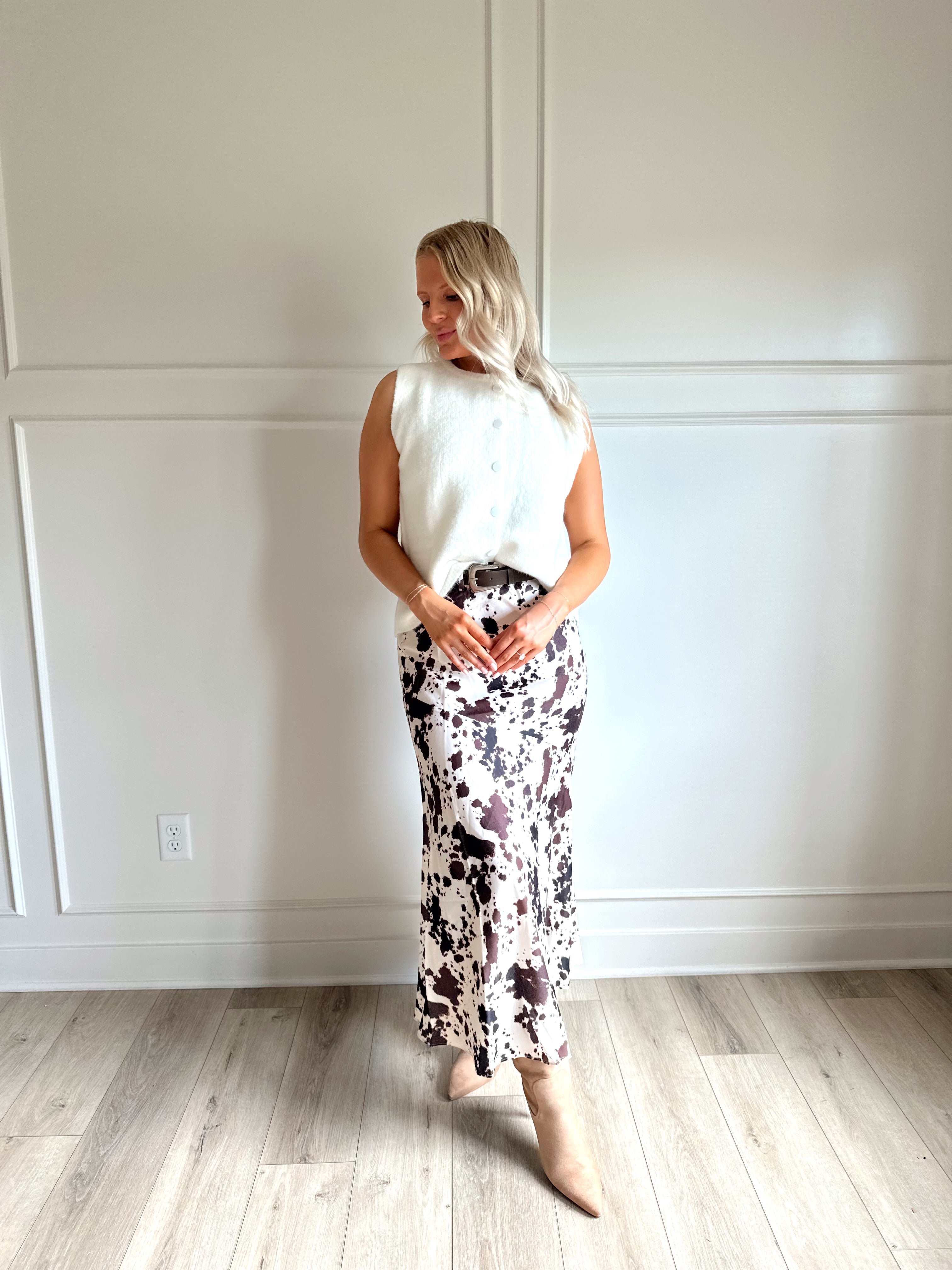 Woman wearing satin cow print maxi skirt with belt detail and white sweater top.