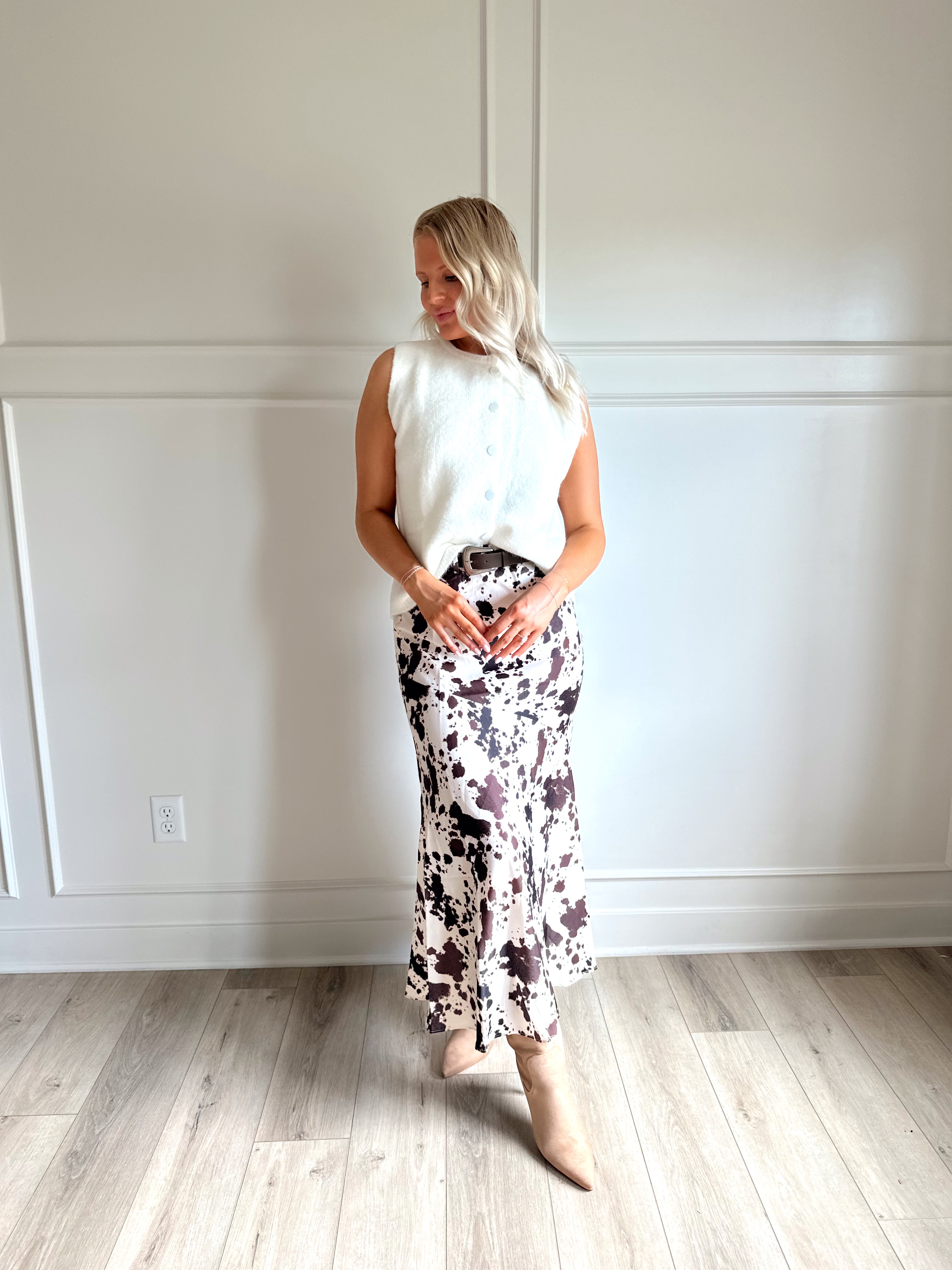 Woman wearing satin cow print maxi skirt with belt detail and white sweater top.